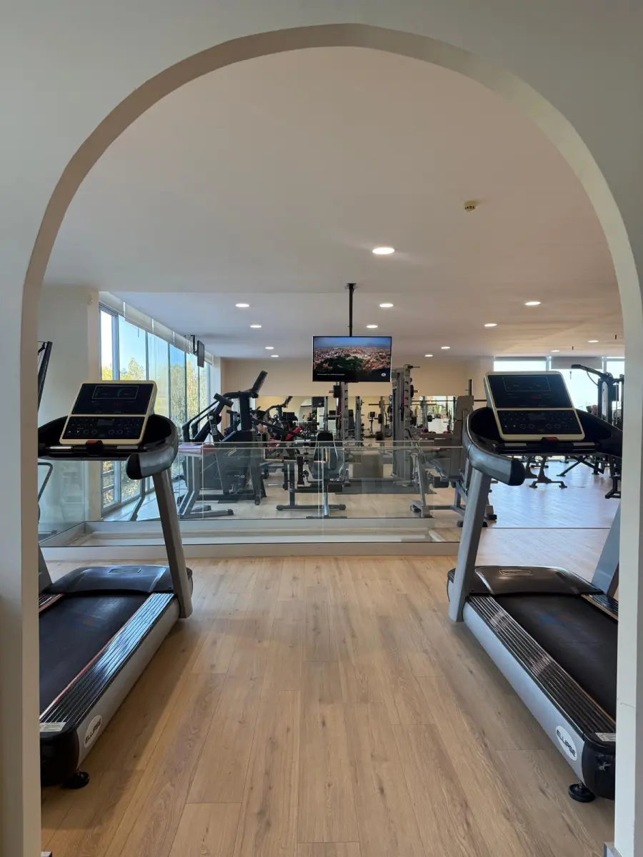 A Sala de musculação vista pelo arco da entrada, com duas passadeiras à frente e as máquinas ao fundo.